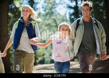 Lächelnde Familie hält die Hände und läuft im Wald Stockfoto