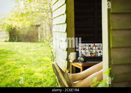 Mann mit Laptop, der Videokonferenz aus dem Gartenhaus genießt Stockfoto