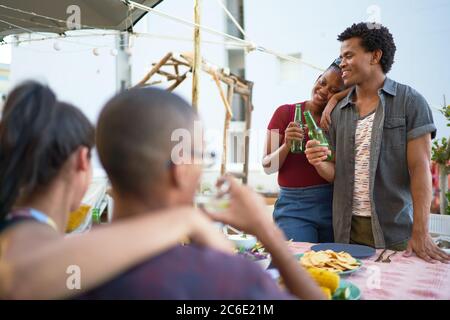 Glückliche junge Freunde, die Bier trinken und am Tisch auf der Terrasse essen Stockfoto