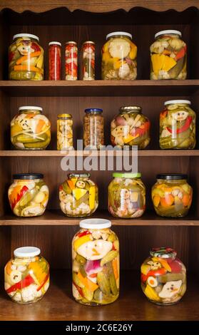 Startseite Einkannen von Sommergemüse auf Holzregalen gelagert. Großmutters Hausmachern - verschiedene Gemüsekonserven, die in Reihen von Glasgefäßen aufgereiht sind. Stockfoto