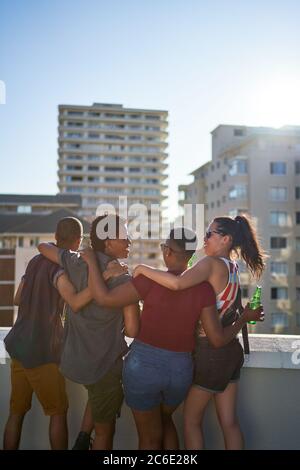 Glückliche junge Freunde, die auf dem sonnigen städtischen Dachbalkon hängen Stockfoto