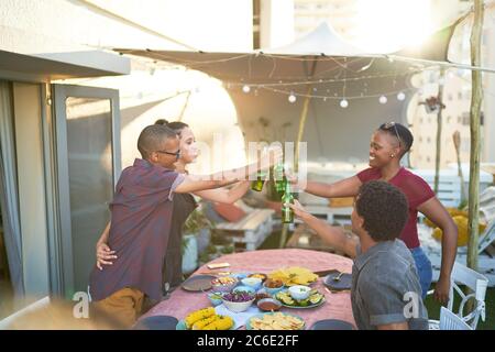 Fröhliche junge Freunde, die Bier über dem Tisch auf der Terrasse toasten Stockfoto