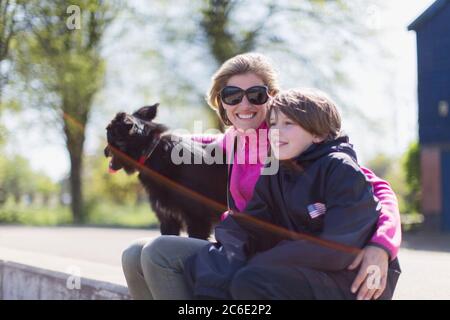 Portrait glückliche Mutter und Sohn mit Hund auf sonniger Kante Stockfoto
