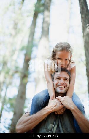 Lächelnder Vater, der die Tochter auf den Schultern in den Wäldern trägt Stockfoto