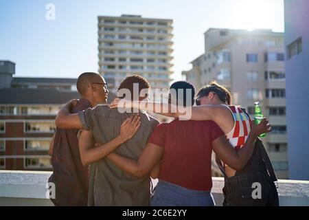 Junge Freunde umarmen sich auf dem sonnigen städtischen Dachbalkon Stockfoto