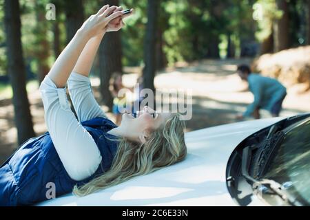 Begeisterte Frau, die Selbstporträt auf Haube des Autos in Wäldern Stockfoto