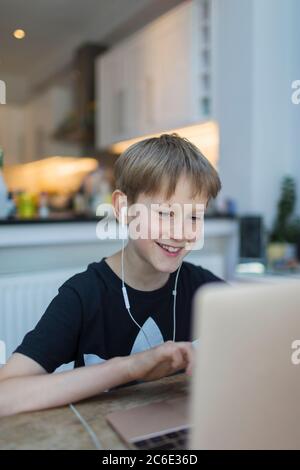 Lächelnder Junge mit Kopfhörern, der am Laptop zuhause ist Stockfoto