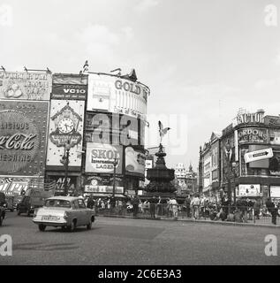 1960er Jahre, historisch, ein Ford Anglia Auto auf dem Piccadilly Circus im Londoner West End, als es ein funktionierender Kreisverkehr war. Die Menschen umgeben den Brunnen der shaftsbury-Gedenkstätte, der gemeinhin als Eros-Statue bekannt ist. Werbetafeln für die großen Marken dieser Zeit sind zu sehen, darunter der BOAC VC10, Skol Lager, Gordons Gin und Wrigleys Kaugummi. Stockfoto