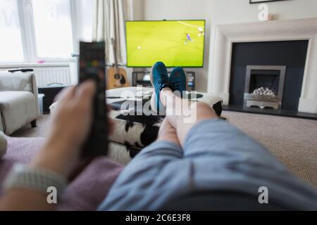 POV Mann auf dem Sofa mit Fernbedienung beobachten Fußballspiel im Fernsehen Stockfoto