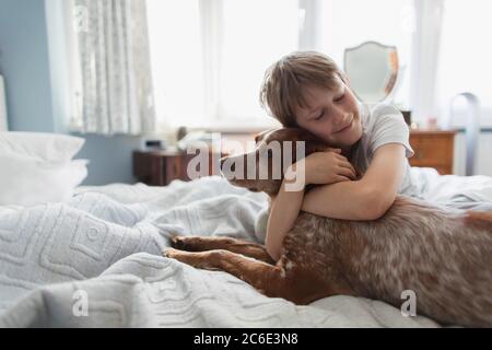 Niedlicher Junge umarmenden Hund auf dem Bett Stockfoto