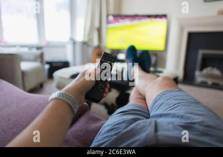 POV Mann mit Fernbedienung beobachten Fußballspiel auf Wohnzimmer Sofa Stockfoto