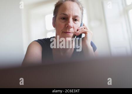 Frau, die am Telefon spricht und am Laptop arbeitet Stockfoto