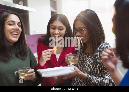 Glückliche indische Frauen essen und trinken Tee in der Küche Stockfoto