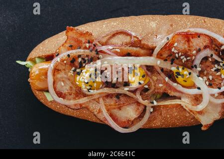 Großes Hotdog mit Wurst, Tomaten, Senf und Salat auf schwarzen Hintergrund isoliert. Ansicht von oben. Stockfoto