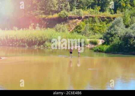 Zwei nicht erkennbare Männer ruhen am Fluss, stehen mit dem Rücken zu den Untiefen in der Ferne Stockfoto