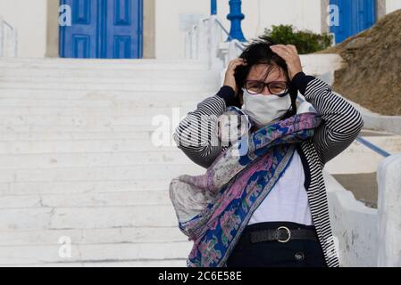 Reife Frau schützt sich vor dem Wind vor einer Kirche in Mascara Stockfoto