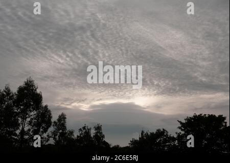 Altocumulus und niedriger Nimbostratus auf einer sehr grauen und übergegossenen Skyline vor Sonnenuntergang mit drohender verschnallter Front, die sich einzieht Stockfoto