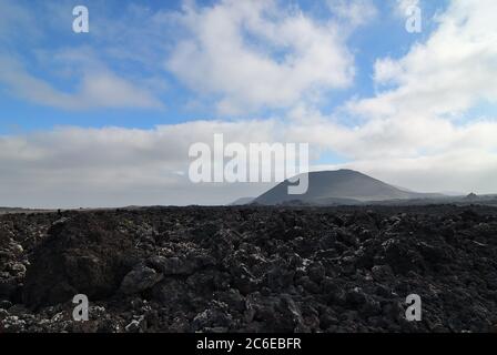 Die weite Leere und Einsamkeit der Lanzarote schwarz gefrorenen Lava vulkanischen Wüste und ein Vulkan im Hintergrund. Lanzarote, Kanarische Inseln. Spai Stockfoto