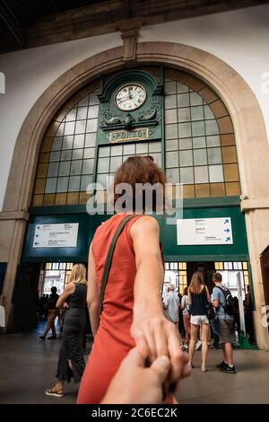 Junge Frau in rotem Kleid hält Hand und geht zum Bahnhof Sao Bento in Porto, Portugal. Follow Me-Konzept. Stockfoto