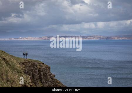 Ein Paar steht am Rand der Klippen bei Lealt auf der Halbinsel Trotternish und blickt über den Sound von Raasay auf die Insel und das Festland beyo Stockfoto