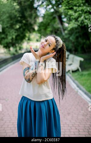 Kreative Hipster Mädchen mit Dreadlocks und Tattoos in einem Stadtpark an sonnigen Sommertag. Junge stilvolle Mädchen mit Dreadlocks im Freien Stockfoto