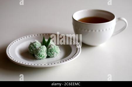 Klepon und eine Tasse Getränk. Klepon ist ein traditioneller Pandanus Reisbällchen aus klejeweidem Mehl und geriebener Kokosnuss mit Palmzucker-Füllung. Indonesisch Stockfoto