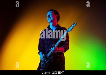 Sommerzeit. Junge inspirierte und expressive Musiker, Gitarrist auf gradienten farbigen Hintergrund in Neonlicht. Konzept der Musik, Hobby, Festival, Kunst. Fröhliche Künstler, bunt, helles Porträt. Stockfoto