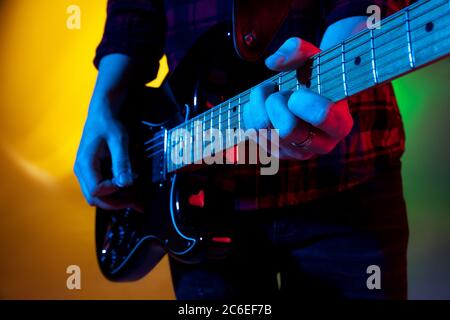 Nahaufnahme junger inspirierter und ausdrucksstarker Musiker, Gitarrist, der auf einem gradienten farbigen Hintergrund in Neonlicht auftrat. Konzept der Musik, Hobby, Festival, Kunst. Fröhliche Künstler, bunt, helles Porträt. Stockfoto