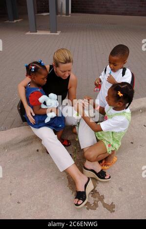 Austin, Texas, USA, 10. September 2005: White Woman unterhält Black Children vor dem Austin Convention Center, während ihre Eltern auf Hilfe warten. Dutzende von Freiwilligen und Mitarbeitern des Roten Kreuzes kämpfen 12 Tage nach dem Niedergang des Sturms an der Golfküste um die Unterstützung Tausender Opfer des Hurrikans Katrina auf der Rettungsstelle in der Innenstadt. ©Bob Daemmrich Stockfoto