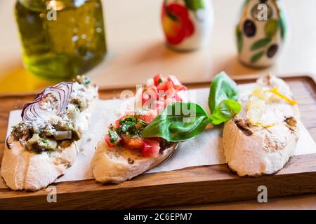 Italienische Bruschetta mit gerösteten Tomaten, Pilzen, Mozzarella-Käse und Basilikumblättern auf einem Holzbrett Stockfoto