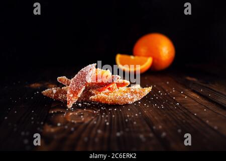 Orangenschalen in Zucker. Kandierte Frucht von Aplsin. Orangefarbene Marmelade auf einem braunen Holztisch mit schwarzem Hintergrund. Orange Geschnitten. Leerer Raum für den Punkt Stockfoto