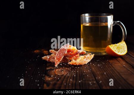 Orangenschalen in Zucker. Kandierte Früchte aus Orange. Orangefarbene Marmelade auf einem braunen Holztisch mit schwarzem Hintergrund. Tee mit Orangenscheiben. Leerumrahmt Stockfoto
