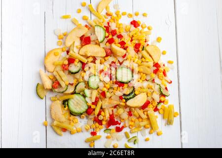 Gemüse gefrorene Mischung zum Braten. Gefrorene Zucchini, Kartoffeln, Mais, Bohnen, Paprika, Zwiebeln auf weißem Holzhintergrund. Schnelle Diät Abendessen. Stockfoto