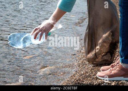 Volunteer zieht eine Plastikflasche aus dem Meer. Konzept der Erhaltung der Ökologie und der Umweltfreundlichkeit. Nahaufnahme. Stockfoto