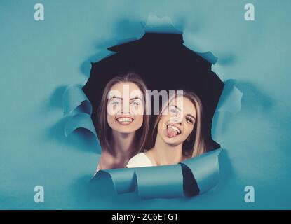 Schöne Mädchen gucken aus einem Loch in blau zerrissenem Papier auf dunklem Hintergrund. Stockfoto