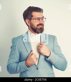 Charmanter junger Geschäftsmann, der seine Jacke aufknöpft, während er einen blauen Anzug trägt. Stockfoto