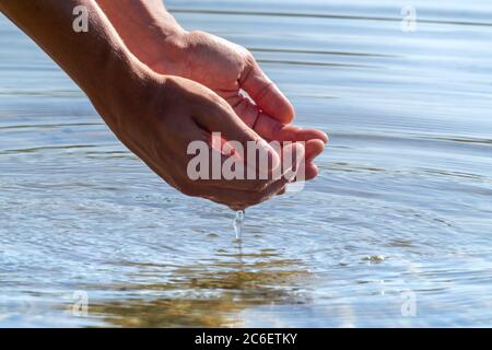 Nahaufnahme der Hände, die Wasser halten, mit Reflexion. Das Anfassen von reinem Wasser in den Händen fällt in die Wasseroberfläche Stockfoto