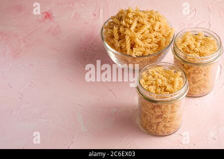 Rohe Weizen goldene Spirale Pasta in Glas Schüssel und Glas auf strukturiertem rosa Hintergrund, Winkel Ansicht kopieren Raum Stockfoto