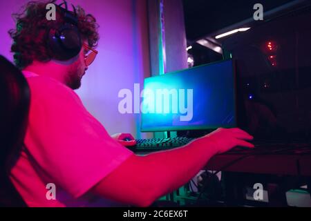 Cybersport. Copyspace auf Monitor, Bildschirm. Voll konzentriert professionelle Gamer spielen wichtige Spiel. Kaukasischer Mann praktiziert vor Turnier allein in Neonlicht. E-Sport, Gamer, Streamer. Stockfoto