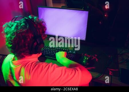 Cybersport. Copyspace auf Monitor, Bildschirm. Voll konzentriert professionelle Gamer spielen wichtige Spiel. Kaukasischer Mann praktiziert vor Turnier allein in Neonlicht. E-Sport, Gamer, Streamer. Stockfoto