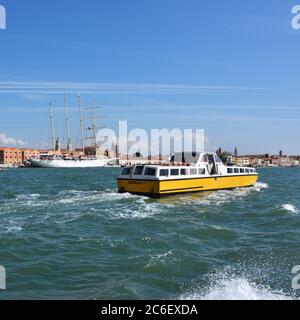 Venedig, Italien - 24. September 2014: Blick auf das gelbe Boot, das die Lagune von Venedig bei Sonnenaufgang überquert, Kreuzfahrtschiff im Hintergrund. Touristen aus der ganzen Welt genießen t Stockfoto