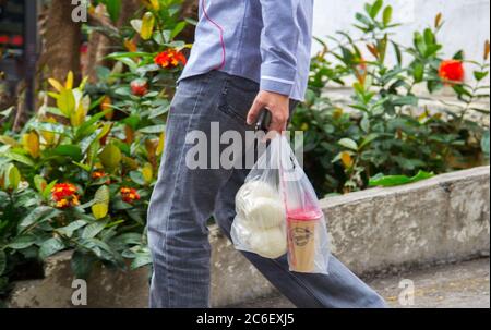 Shenzhen, China - November 24 2018: Yuong Mann trägt Snacks von Kaffee und Brot in wegwerfenden Plastiktüten. Rücksichtsloser Verbrauch von pl Stockfoto