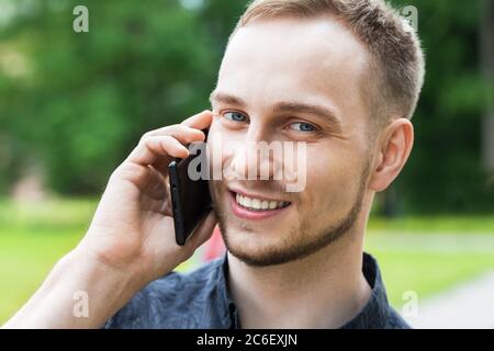 Porträt eines hübschen jungen Mannes, der im Park spazierengeht und auf dem Handy spricht. Mann, der auf dem Handy spricht, Nahaufnahme. Stockfoto
