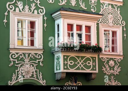 Fassade eines schönen grünen Barockhauses in Scharding, Österreich mit einem kleinen Erker, der mit rosa Geranienblumen geschmückt ist. Stockfoto