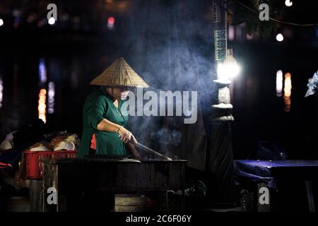 Frau mit vietnamesischem Hut Kochen auf einem Grill in der Nacht Stockfoto