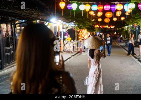 Asiatische Frau, die während der hoi an Nacht eine Frau in weißem vietnamesischem Kleid auf der Straße fotografiert Stockfoto