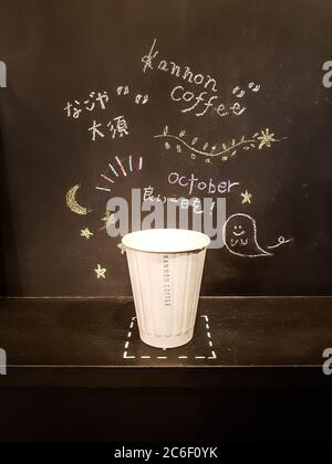 Nagoya, Aichi, Japan - EINE Tasse Kaffee an Halloween. Eine Take-out Tasse in einem Hintergrund aus schwarzen Wand mit Hand Schreiben und Malerei verziert. Stockfoto