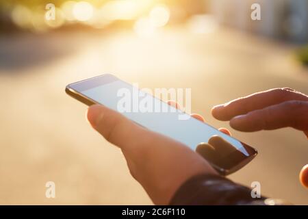 Mann, der sein Mobiltelefon im Freien benutzt, Nahaufnahme. Mann hält Smartphone mit verschwommenem Hintergrund. Stockfoto