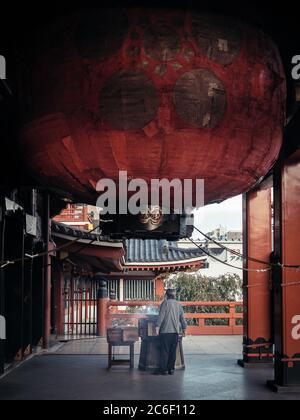 Nagoya, Aichi, Japan - ein alter Mann, der eine Kultfeier unter der riesigen roten japanischen Laterne in Osu Kannon hat. Buddhistischer Tempel in Ōsu. Stockfoto