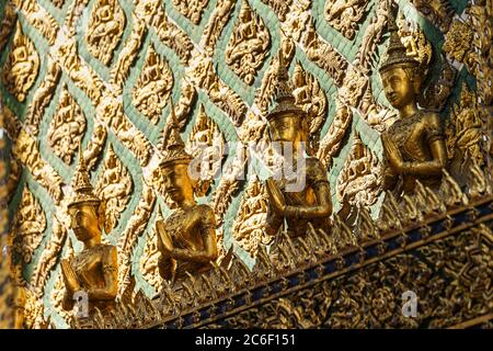 Mehrere goldene Statuen beten, lehnen sich an die grüne und goldene Wand im Hintergrund Stockfoto